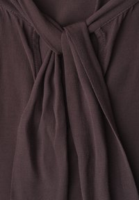 Tissu marron foncé avec un design plissé noué en un nœud, montrant la texture et les détails de couture sur le matériau doux.