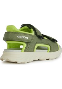 Zelené a černé sandály s suchým zipem, síťovinovou podšívkou a perforovanými vzory. Silná bílá podešev pro odpružení a podporu.