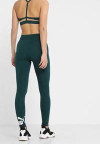 Turkusowy stanik sportowy z wąskimi ramiączkami i wycięciami, zestawiony z pasującymi turkusowymi legginsami z białym logo na kostce.