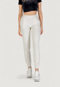 Jogger grigi chiari con vita e polsini elasticizzati, materiale morbido, dettaglio logo discreto sull'anca, abbinati a sneakers bianche.