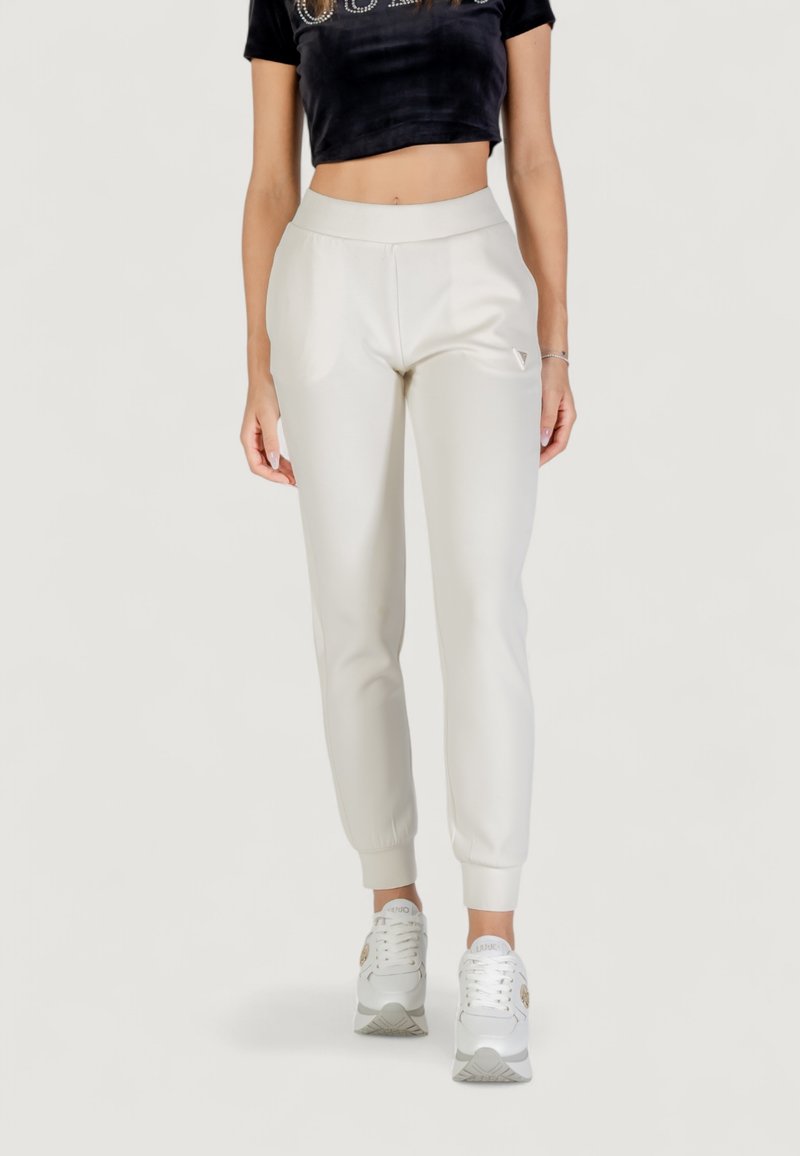 Jogger grigi chiari con vita e polsini elasticizzati, materiale morbido, dettaglio logo discreto sull'anca, abbinati a sneakers bianche.
