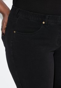 Vaqueros de mezclilla negra de corte ajustado, con bolsillos frontales, detalles en hardware dorado y una cinturilla texturizada.