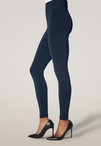 Marina leggings gjorda av elastiskt tyg med hög midja, tillsammans med svarta högklackade skor med spetsig tå-design.