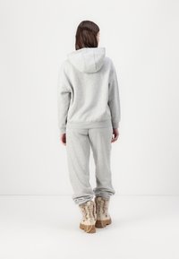 Pantaloni de jogger gri și hanorac cu glugă dintr-o țesătură moale. Gluga dispune de un șnur de strângere. Modelul poartă cizme bej cu accente din blană.