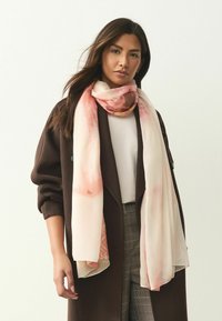 Gaisīgs rozā un krēmkrāsas šalle ar smalku ziedu rakstu, apskauta ap kaklu, ar mīkstu tekstūru un pušķainām malām.