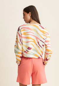 Felpa croppata multicolore con un motivo ondulato nelle tonalità di rosa, arancione e verde. Abbinata a pantaloni corti di cotone rosa, dal tessuto liscio.