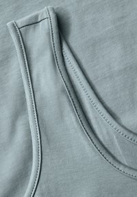 Närbild av ljusblått tyg som visar detaljerad sömnad och sömmar på ett ärmlöst plagg, troligtvis en linne.