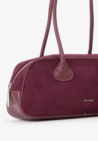 Borsa bordeaux in suede con dettagli in pelle, dotata di chiusura con zip, due manici e un dettaglio logo in argento. Texture morbida.