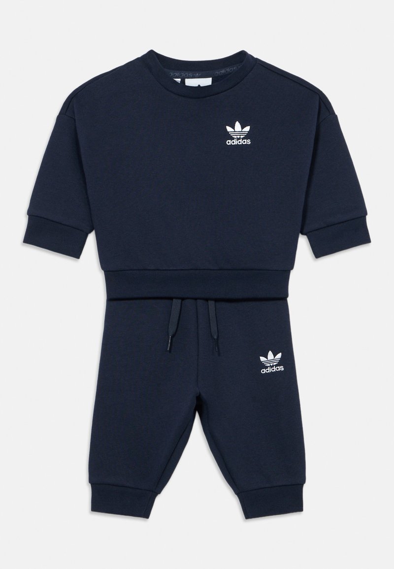 Conjunto de sweatshirt e calças de fato de treino azul marinho feito de tecido macio. Apresenta um logo Adidas branco no peito e na perna esquerda da calça. Punhos e cintura elásticos.