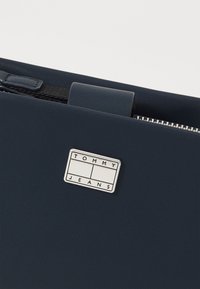 Plic de document sintetic de culoare bleumarin, cu un finisaj texturat. Previne un logo argintiu "TOMMY JEANS" și un sistem de închidere cu fermoar.