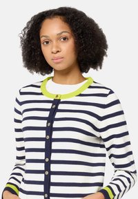 Sweter w paski w kolorze granatowym i białym, z jaskrawozielonym kołnierzem. Posiada długie rękawy i ozdobne guziki z przodu.