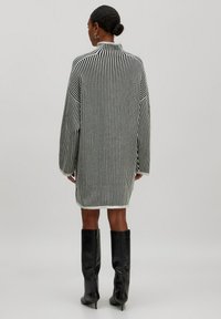 Robe pull oversize à rayures noires et blanches avec un col montant, des manches larges et un ourlet qui tombe au-dessus du genou.