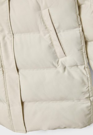 Doudoune en beige clair. Features un design matelassé, une poche intérieure et un tissu synthétique lisse avec une finition mate.