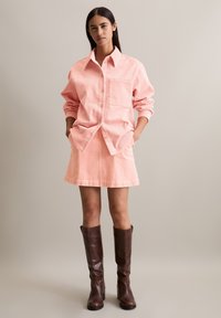 Roze corduroy overhemd met een zak, gecombineerd met een bijpassende corduroy rok. Bruine leren kniehoge laarzen maken de outfit compleet.