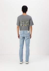 Grå t-skjorte med et kaktusmotiv på baksiden, parret med lyseblå jeans. Jeansene har et nøye utformet baklomme-design.