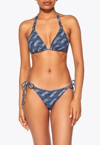 Bikini a motivo denim con top triangolare, spalline a halter e slip con laccetti ai lati. Presenta un design tessuto con una trama in tonalità di blu scuro.