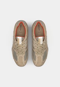 Beige sneakers med mesh- og semsket overdel, rund tå, snøring, og røde detaljer på innsiden. Har logo og perforerte detaljer.