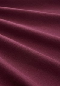 Tissu bordeaux lisse avec des plis délicats créant des ombres douces et une texture à la surface.