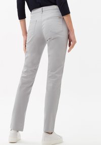 Pantalons gris clair avec une coupe slim, en tissu lisse. Présente une taille mi-haute, des poches arrière et des détails de couture subtils.