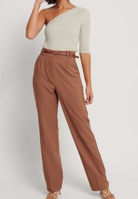Top a costine di colore verde chiaro con una spalla, abbinato a pantaloni marroni a gamba larga e alta vita, accentuato da una cintura marrone e sandali con cinturini.