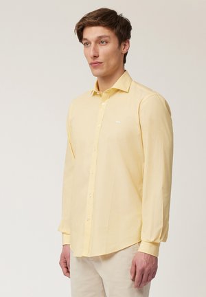 Gele langslung shirt met een button-down kraag en een klein wit logo op de borst. Gemaakt van lichte, zachte stof.
