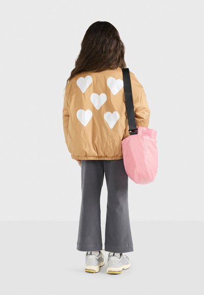 Giacca bomber color tan con motivi a cuore bianchi, pantaloni a zampa d'elefante grigi e una borsa a spalla rosa. Presenta un tessuto morbido e una vestibilità comoda.
