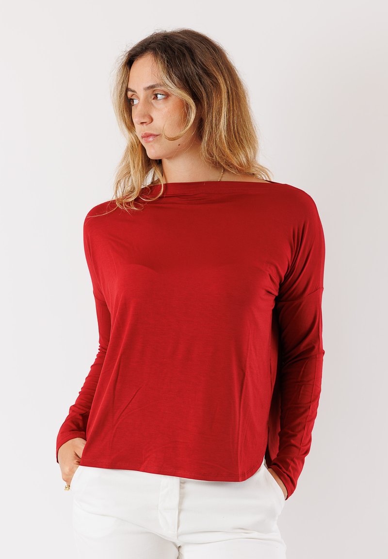 Maglietta rossa a maniche lunghe con vestibilità rilassata e scollo ampio. Realizzata in un tessuto liscio e morbido. Presenta maniche lunghe e orlo leggermente arrotondato.