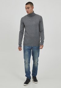 Grå turtleneck sweater med lange ærmer, lavet af blødt materiale, parret med lyseblå jeans og sorte sneakers. Enkelt, tætsiddende design.