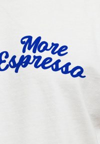Weißes Stoff-T-Shirt mit fettem blauen, kursiven Text "Mehr Espresso". Glatte Oberfläche ohne zusätzliche Muster oder Akzente.