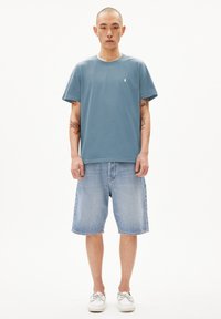 Blauwe katoenen t-shirt met een ronde hals en geborduurd logo, gecombineerd met lichtblauwe denim shorts en witte bootschoenen. Eenvoudig casual ontwerp.