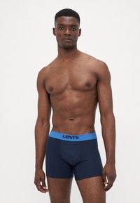 Morske bombažne raztegljive bokserice z modrim elastičnim pasom, ki vsebuje črni napis "Levi's". Utesnjen dizajn, mehak material in dolžina do sredine stegen.