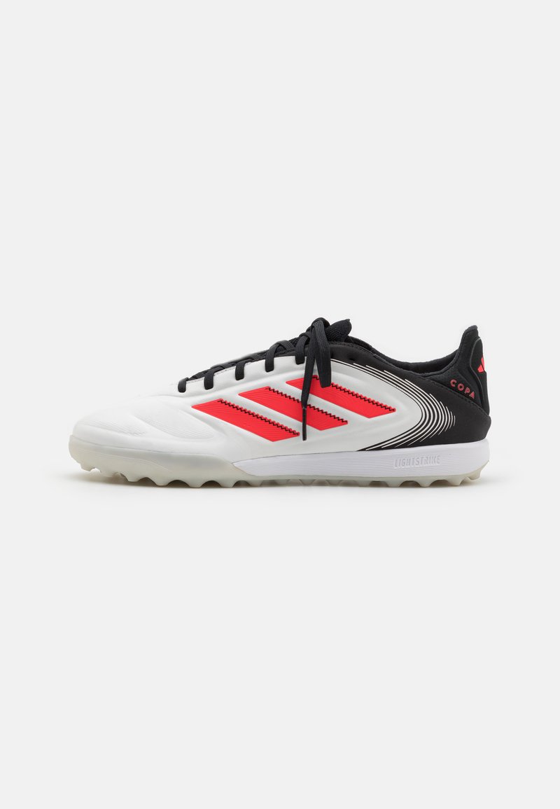 Baskets de sport blanches avec des accents noirs, présentant des rayures rouges, une surface texturée et une semelle extérieure en caoutchouc flexible. Marquage "COPA" sur le talon.