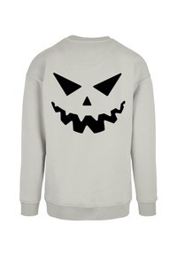Ljust grå sweatshirt med en stor svart, zick-zack-formad smiley-ansiktsgrafik på baksidan. Tillverkad av mjukt tyg med ribbade ärmslut och fåll.