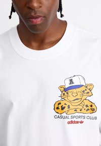White cotton t-shirt featuring a cartoon leopard graphic with a blue cap and black leopard spots. Text below reads "CASUAL SPORTS CLUB" and "adidas."