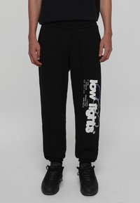 Svarta sweatpants med avslappnad passform, med en vit logotryck på vänster ben. Tillverkade av ett mjukt material, med elastiskt midjeband och ärmslut.