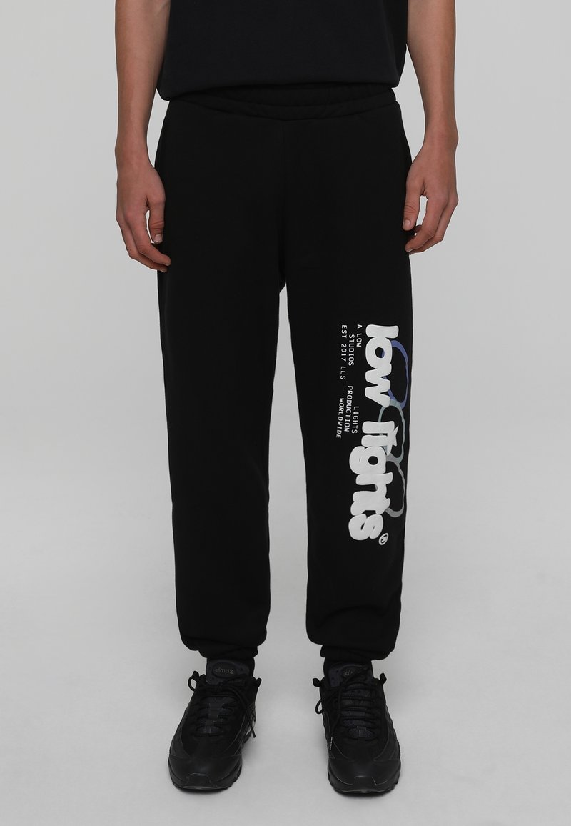 Svarta sweatpants med avslappnad passform, med en vit logotryck på vänster ben. Tillverkade av ett mjukt material, med elastiskt midjeband och ärmslut.