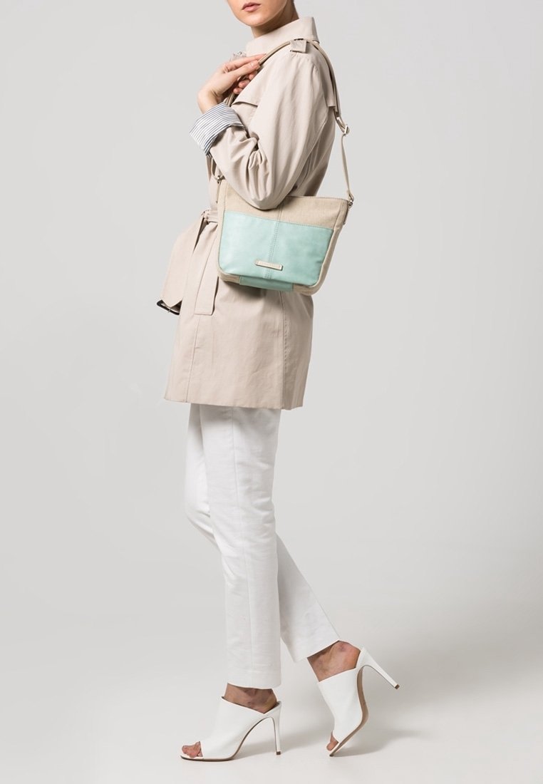 Beige crossbody taske med en turkise panel, prydet med en metaldetalje, båret med en trenchcoat og hvide bukser, stylet med hvide hæle.