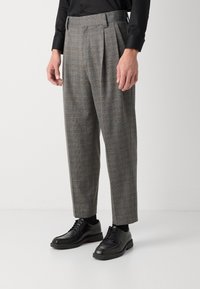 Grau karierte Hose mit hohem Bund und Falten, kombiniert mit schwarzen Schnürschuhen. Glattes Material mit einer taillierten Passform.