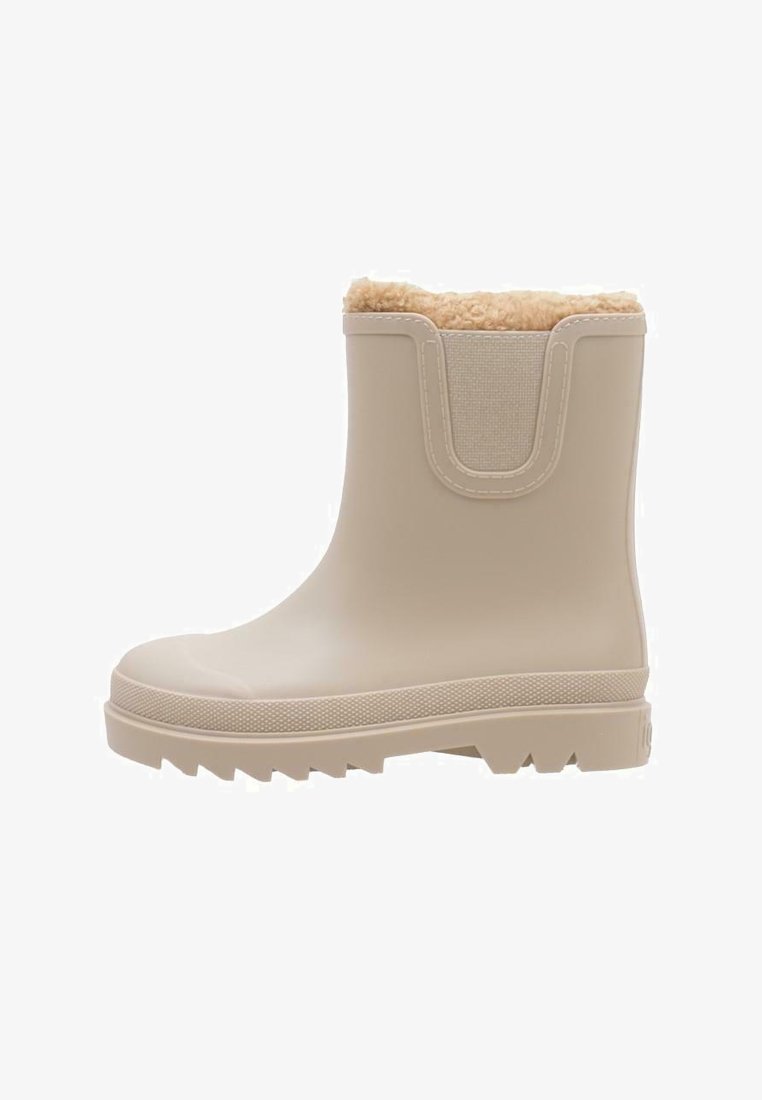 Beige waterproof ankle boot with a textured rubber sole, plush inner lining, and elastic panel for easy wear. Flat, rugged outsole design.