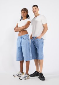 Two models wearing casual outfits: a fitted white T-shirt and light blue denim shorts. The shorts have a relaxed fit and frayed hems.