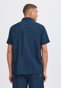 Camisa de manga corta en color marino con un acabado texturizado y cuello estándar. Presenta un corte recto y un ajuste ligeramente holgado. Detalle de yugo trasero visible.