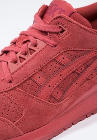 Röd mockasinsneaker med perforerat mönster, texturerade detaljer och flätade snörningar. Signaturbranding på tungan med gummisula.