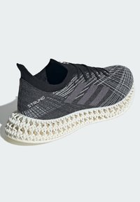 Black athletic shoe with a textured upper, gray accent lines, and a distinctive white lattice-style sole. Features a snug fit and lace closure.