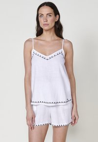 Witte linnen camisole en shorts set met zwart geborduurde details langs de randen en banden. Lichtgewicht stof met een ontspannen pasvorm.