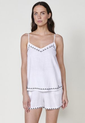 Witte linnen camisole en shorts set met zwart geborduurde details langs de randen en banden. Lichtgewicht stof met een ontspannen pasvorm.