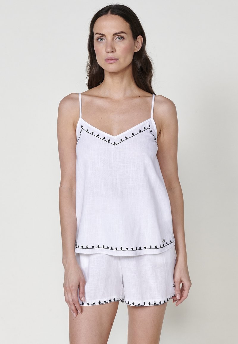 Set di canotta e pantaloni corti in lino bianco con dettagli ricamati neri lungo i bordi e le spalline. Tessuto leggero con una vestibilità comoda.