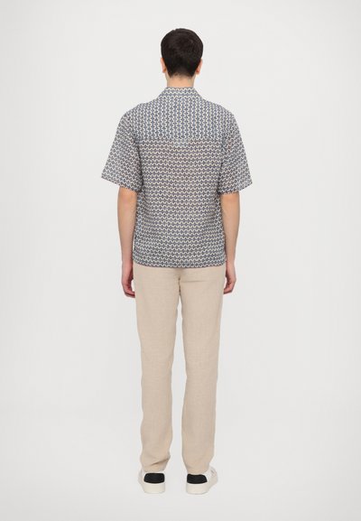 Polokošeľa s krátkym rukávom a modro-bielym geometrickým vzorom, skombinovaná s svetlo béžovými ľanovými nohavicami a bielymi teniskami s čiernymi akcentmi.