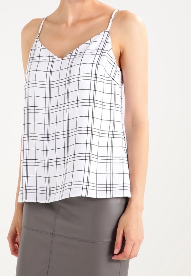 Bílý bezrukávový top s černým mřížkovaným vzorem, V- výstřihem a nastavitelnými tenkými ramínky, kombinovaný se šedou přiléhavou sukni.