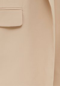 Blazer beige con una texture di tessuto liscia, dotato di una tasca a motivo sul lato sinistro, linee pulite e design minimalista.