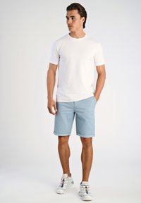 Vit kortärmad t-shirt i kombination med ljusblå rutiga shorts med upprullade ärmar. Bärs med vita sneakers som har färgade detaljer.